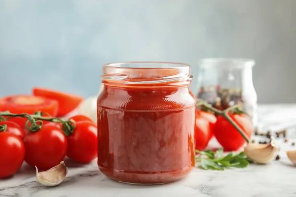 Композиция с банкой вкусного томатного соуса на столе на сером фоне — стоковое фото
