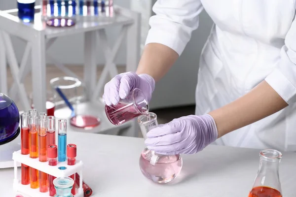 Ученый наливает реагент во фляжку за столом в химической лаборатории — стоковое фото