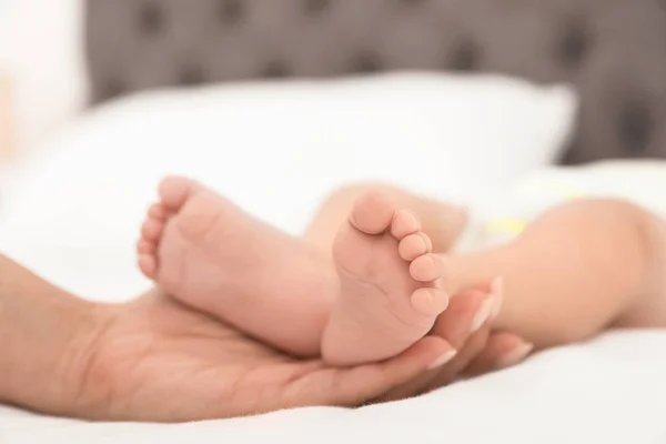 Mamma håller barnets fötter på sängen, närbild — Stockfoto