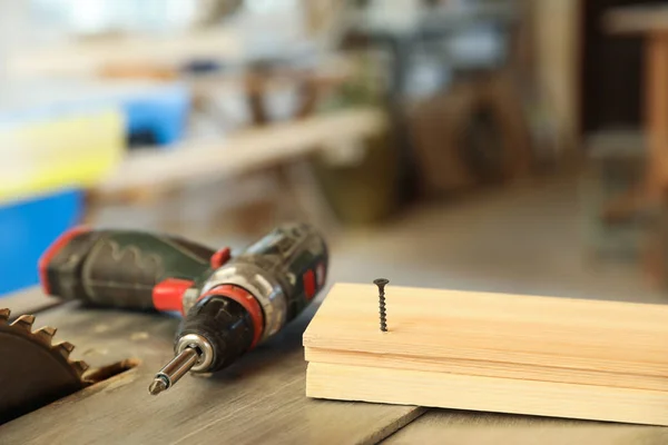 Lugar de trabajo del carpintero con destornillador eléctrico y tira de madera en la mesa en interiores — Foto de Stock