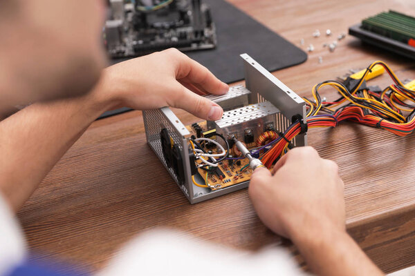 Male technician repairing power supply unit at table, closeup