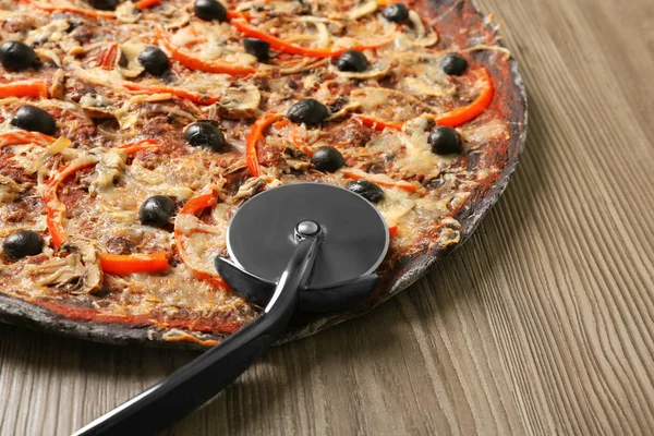 Black pizza and knife on wooden table, closeup