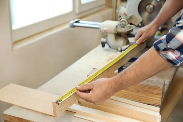 Hombre trabajador midiendo tira de madera en carpintería, primer plano — Foto de Stock