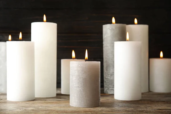 Muitas velas de cera acesas na mesa contra fundo escuro — Fotografia de Stock