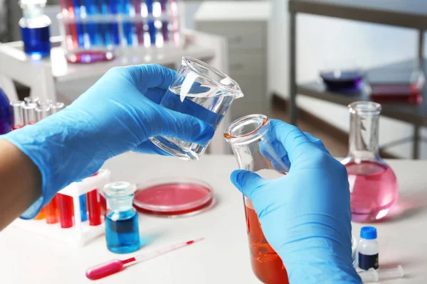 Ученый наливает реагент в стакан за столом в химической лаборатории, крупным планом — стоковое фото