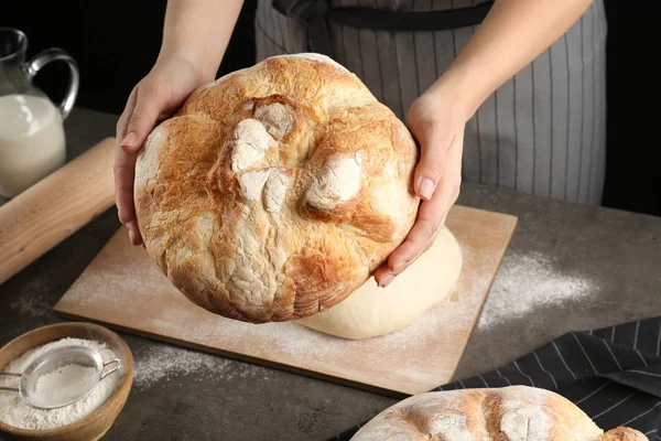 Fêmea padeiro segurando pão sobre mesa de cozinha, close-up — Fotografia de Stock