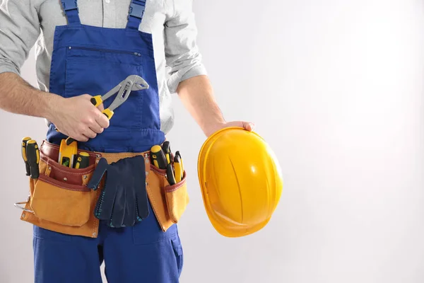 Trabalhador da construção civil com instrumento, chapéu duro e cinto de ferramentas em fundo leve, close-up. Espaço para texto — Fotografia de Stock