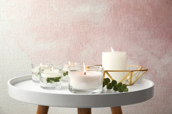 Composition with burning aromatic candles and eucalyptus on table near color wall. Space for text — Stock Photo, Image