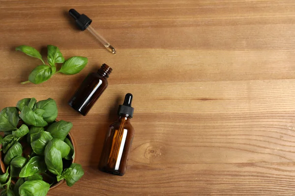 Flat lay composition with bottles of essential oil, basil and space for text on wooden background — Stock Photo, Image