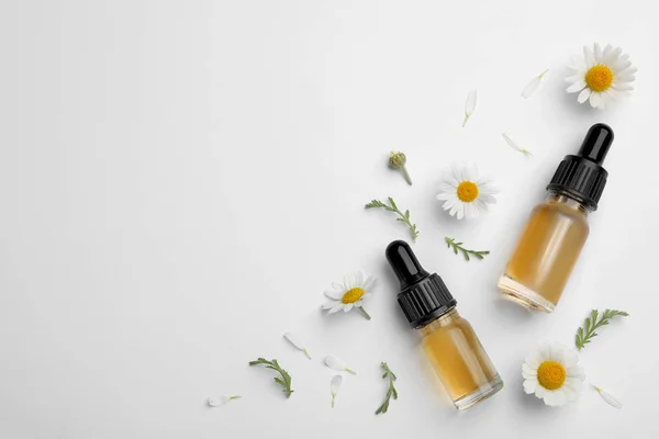 Composizione con fiori di camomilla e bottiglie cosmetiche di olio essenziale su fondo bianco, vista dall'alto — Foto Stock