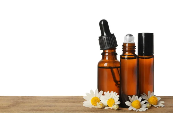 Kamillenblüten und Kosmetikflaschen mit ätherischem Öl auf einem Holztisch vor weißem Hintergrund. Raum für Text — Stockfoto