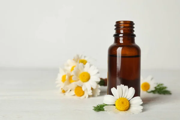 Kamillenblüten und Kosmetikflasche mit ätherischem Öl auf Holztisch vor hellem Hintergrund. Raum für Text — Stockfoto