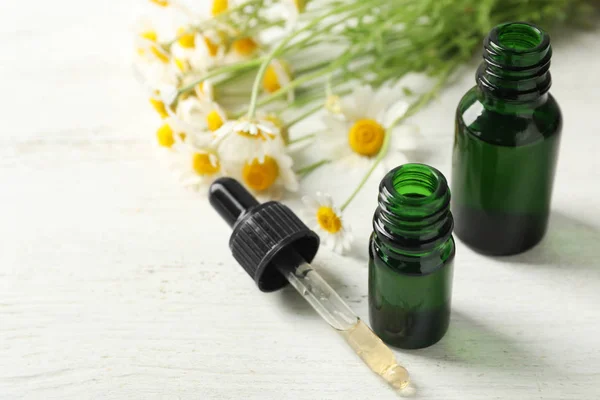 Chamomile flowers and cosmetic bottles of essential oil on wooden table, closeup. Space for text — Stock Photo, Image
