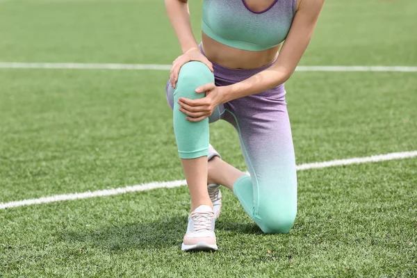 Vrouw in sportkleding die lijden aan knie pijn op voetbalveld, close-up — Stockfoto
