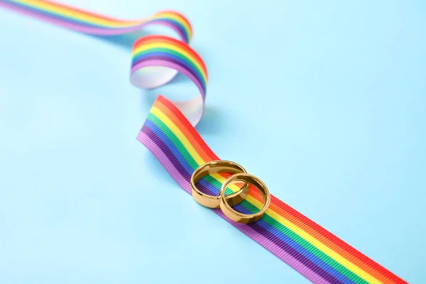 Trouwringen en regenboog lint op kleur achtergrond. Gay symbool — Stockfoto
