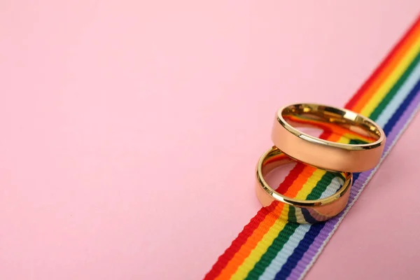 Trouwringen en regenboog lint op kleur achtergrond, ruimte voor tekst. Gay symbool — Stockfoto