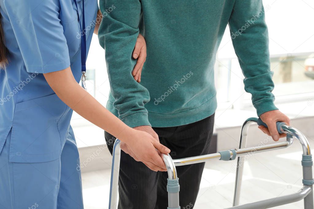 Nurse assisting senior man with walker in hospital, closeup