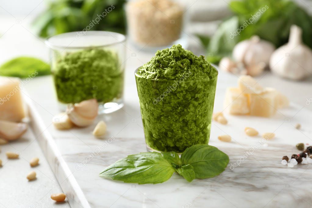 Board with glass of pesto sauce and basil on table