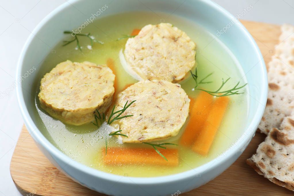 Board with bowl of Jewish matzoh balls soup on table, closeup