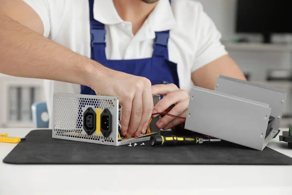 Male technician repairing power supply unit at table indoors, closeup — Stock Photo, Image