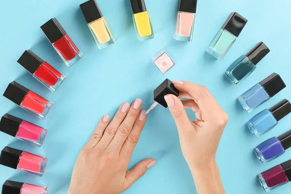 Woman applying nail polish on color background, above view