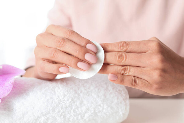 Woman removing polish from nails with cotton pad at table, closeup