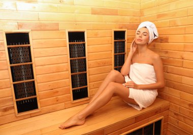 Kızıl ötesi saunada ahşap bankta oturan genç bir kadın, mesaj için yer var. Spa tedavisi