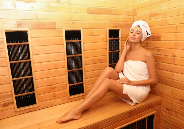 Young woman sitting on wooden bench in infrared sauna, space for text. Spa treatment — Stock Photo, Image