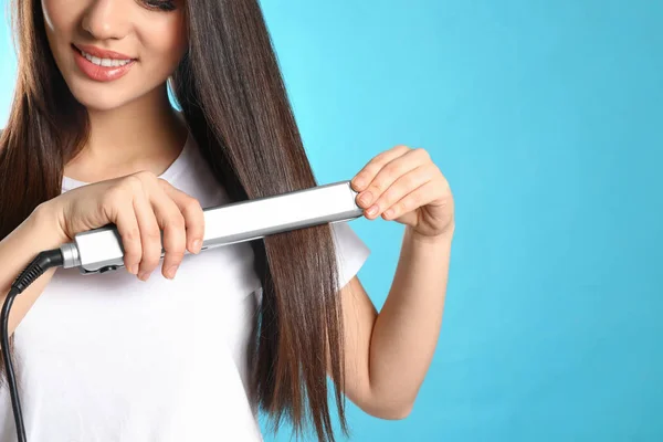 Happy woman using hair iron on color background, closeup. Space for text