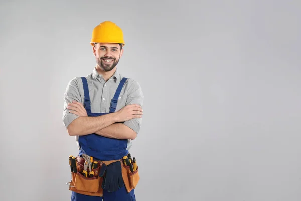 Portrait of professional construction worker with tool belt on grey background, space for text — Stock Photo, Image