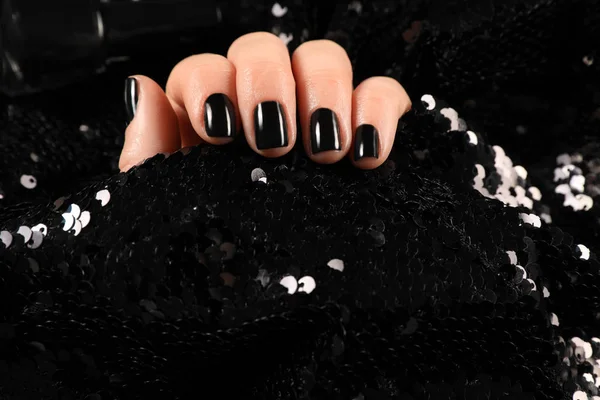 Woman with black manicure holding shiny fabric, closeup. Nail polish trends