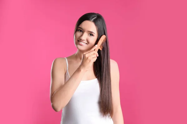 Mooie lachende jonge vrouw met haar kam op kleur achtergrond — Stockfoto