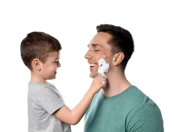 Pequeno filho aplicando espuma de barbear no rosto do pai contra o fundo branco — Fotografia de Stock