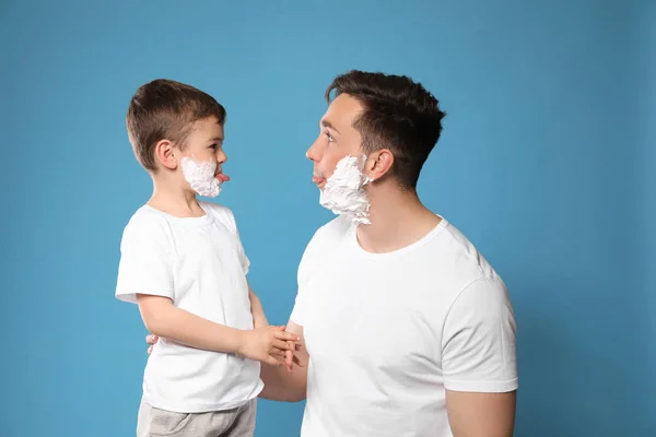 Papá y su hijo pequeño con espuma de afeitar en las caras contra el fondo de color — Foto de Stock