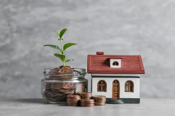 Modèle de maison, pot avec des pièces de monnaie et plante sur la table sur fond gris. Espace pour le texte — Photo