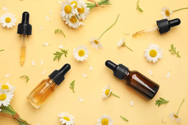 Composição de leigos planos com flores de camomila e garrafas cosméticas de óleo essencial sobre fundo de cor — Fotografia de Stock