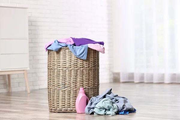 Laundry basket with dirty clothes and detergent on floor in room, space for text — Stock Photo, Image