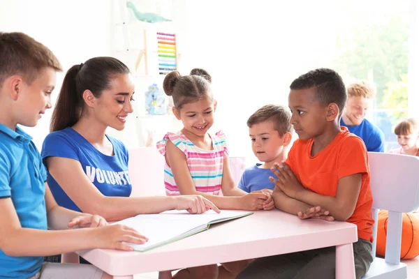 Молодой волонтер читает книгу с детьми за столом в помещении — стоковое фото