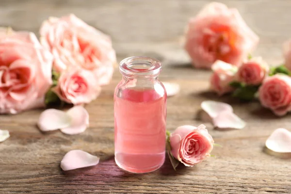 Garrafa de óleo essencial de rosa e flores na mesa de madeira — Fotografia de Stock