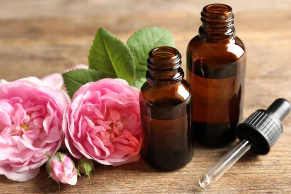 Flessen rozen etherische olie, pipet en bloemen op houten tafel — Stockfoto