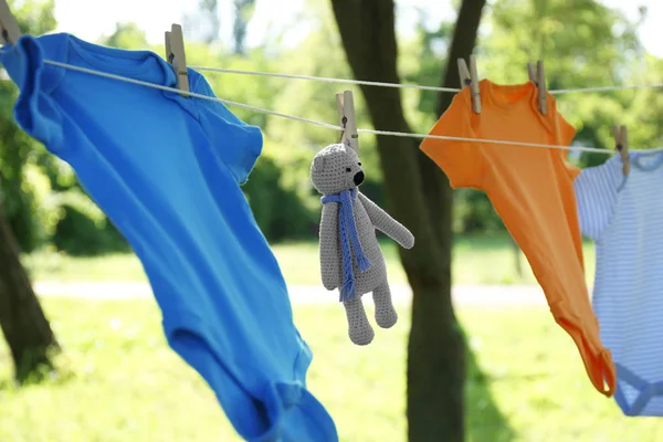 Barevné dětské onesie a medvěd hraček visící na vnější straně oděvu — Stock fotografie