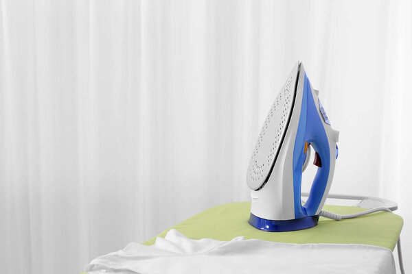 Modern electric iron and t-shirt on board indoors, space for text. Laundry day
