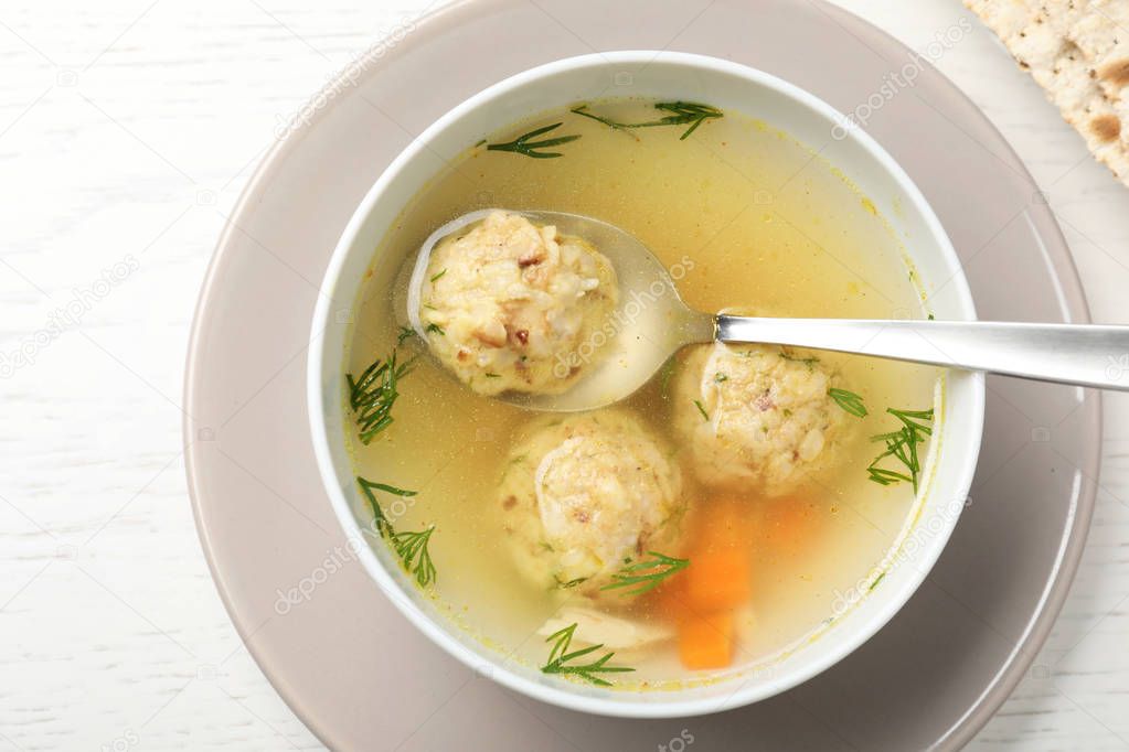Bowl of Jewish matzoh balls soup on white wooden table, top view