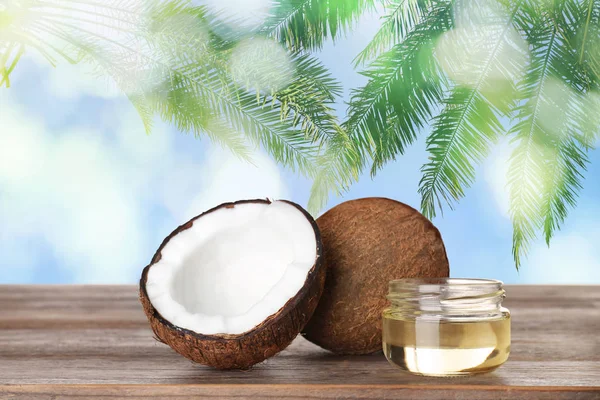 Kokosnoten en natuurlijke organische olie op houten tafel tegen tropische palmbladeren — Stockfoto