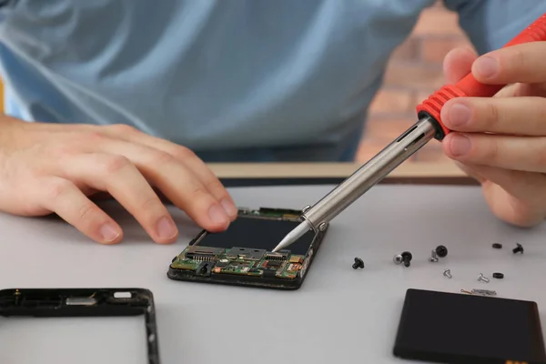 Техник чинит сломанный смартфон за столом, крупным планом — стоковое фото