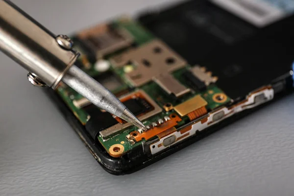 Repairing broken smartphone with soldering iron on table, closeup. Space for text