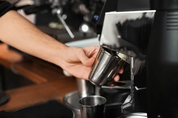 Barista with metal cup using coffee grinding machine in cafe, closeup — Stock Photo, Image