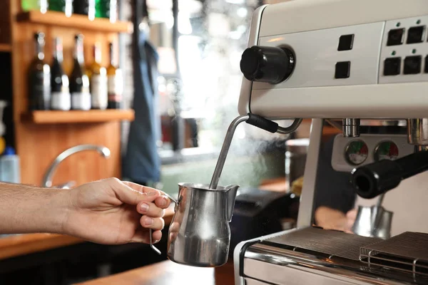 Barista steaming milk in metal jug with coffee machine wand at bar counter, closeup — Stock Photo, Image