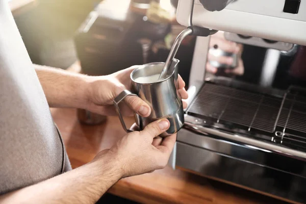 Barista frothing milk in metal pitcher with coffee machine wand at bar counter, closeup — Stock Photo, Image