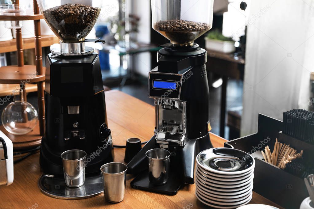 Modern coffee grinding machines with metal cups and saucers on wooden bar counter